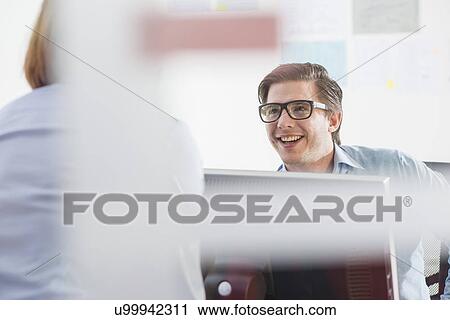 Stock Image - Businessman and woman chatting in office. Fotosearch