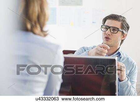 Stock Image - Businessman and woman having informal meeting at office desk. Fotosearch