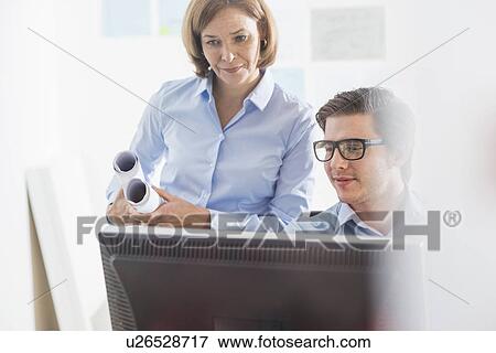 Stock Photo - Businessman and woman looking at computer at office desk. Fotosearch