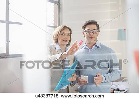 Stock Photo - Businessman and woman pointing at office glass wall. Fotosearch