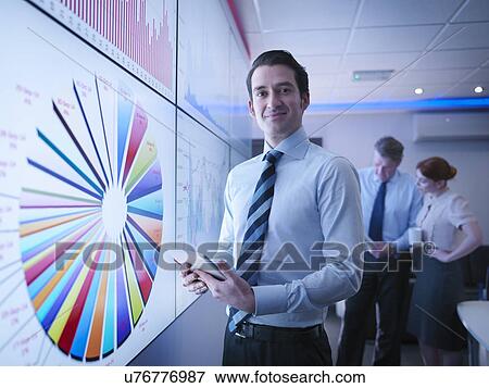 Businessman in front of graphs on screen in meeting room View Large Photo Image Stock Photo - Businessman in front of graphs on screen in meeting room. Fotosearch