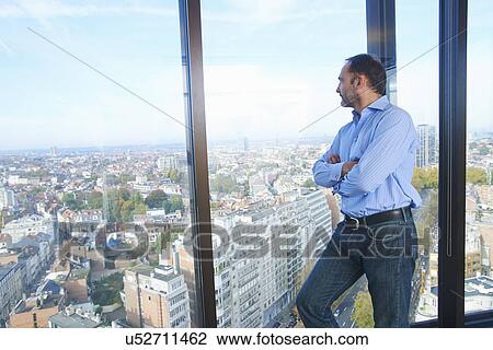 Stock Image - "Businessman looking from office window at Brussels cityscape, Belgium". Fotosearch