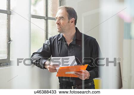 Businessman reading paperwork and gazing out of office window View Large Photo Image Stock Image - Businessman reading paperwork and gazing out of office window. Fotosearch