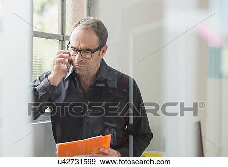 Businessman reading paperwork and chatting on smartphone View Large Photo Image Stock Photo - Businessman reading paperwork and chatting on smartphone. Fotosearch