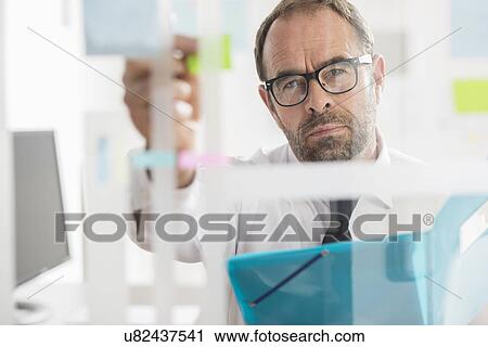 Businessman sticking adhesive notes to glass wall in office View Large Photo Image Stock Image - Businessman sticking adhesive notes to glass wall in office. Fotosearch