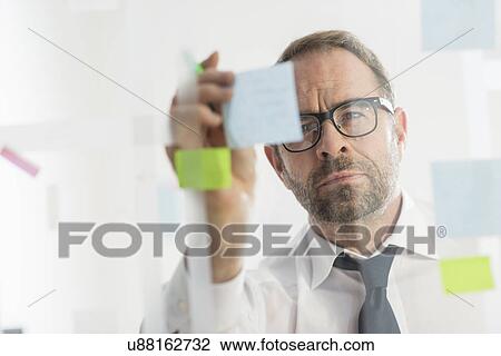 Businessman sticking adhesive notes to glass wall View Large Photo Image Stock Image - Businessman sticking adhesive notes to glass wall. Fotosearch