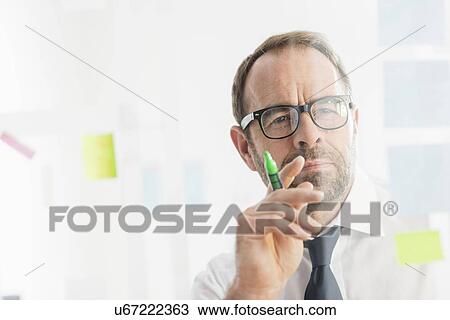 Stock Image - Businessman working on ideas at office glass wall. Fotosearch