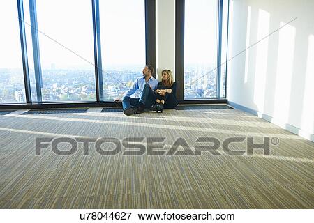 Stock Photo - "Businesswoman and man sitting in front of window in empty skyscraper office, Brussels, Belgium". Fotosearch