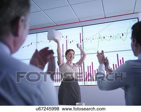 Stock Photo - Businesswoman celebrating success in front of graphs on screen as colleagues applaud. Fotosearch