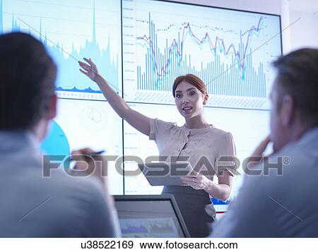 Businesswoman making presentation to colleagues in front of graphs on screen View Large Photo Image Stock Photo - Businesswoman making presentation to colleagues in front of graphs on screen. Fotosearch