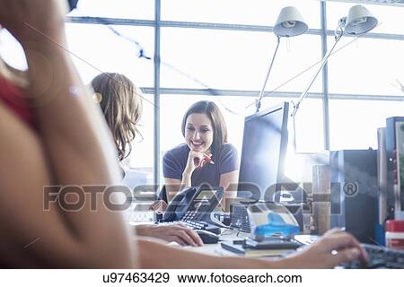 Stock Photo - Businesswomen chatting at office desk. Fotosearch