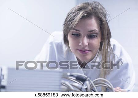 Stock Image - Close up of female scientist in lab using scanning electron microscope. Fotosearch