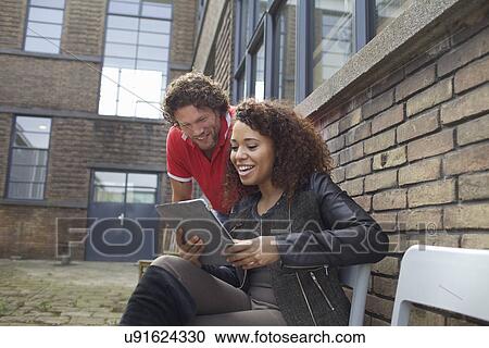 Stock Image - Colleagues looking at digital tablet in office courtyard. Fotosearch