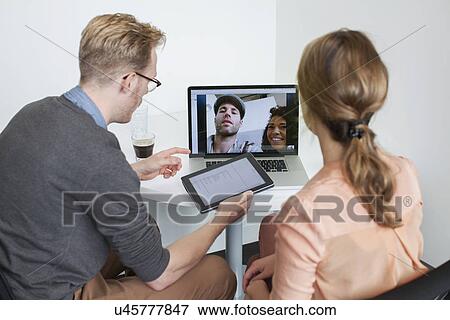 Stock Photo - Colleagues sharing laptop video call with partners. Fotosearch