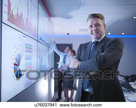 Stock Image - "Company manager in front of graphs on screen in meeting room, portrait". Fotosearch