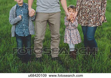 Stock Photo - Cropped shot of young couple with son and daughter strolling in grassy field. Fotosearch