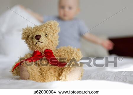 Cute teddy bear sitting up in bed in front of baby girl View Large Photo Image Picture - Cute teddy bear sitting up in bed in front of baby girl. Fotosearch