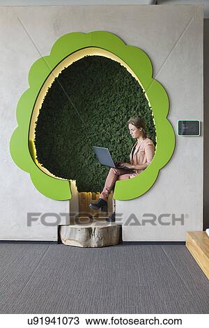 Stock Image - Designer working on laptop in tree shaped office space. Fotosearch