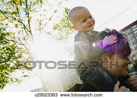Stock Image - Father giving baby daughter shoulder ride whilst walking in city. Fotosearch