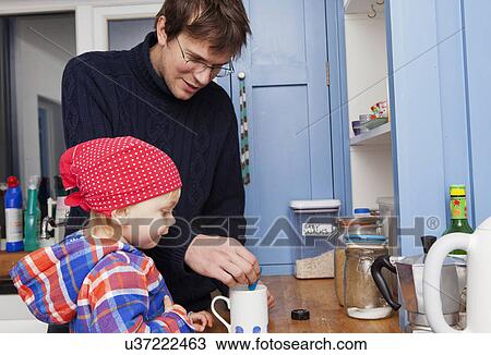 Stock Image - Father making cup of tea with son in kitchen. Fotosearch