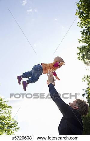 Stock Image - Father throwing baby daughter mid air in park. Fotosearch