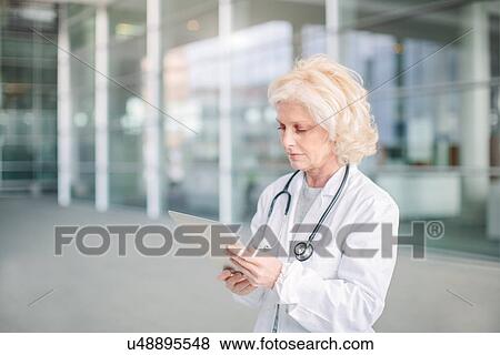 "Female doctor standing outside building, using digital tablet" View Large Photo Image Stock Photo - "Female doctor standing outside building, using digital tablet". Fotosearch