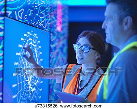 Stock Photograph - Female geologist with colleague studying graphical display of oil and gas bearing rock on screens. Fotosearch