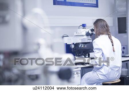 Picture - Female scientist looking through scanning electron microscope in lab. Fotosearch