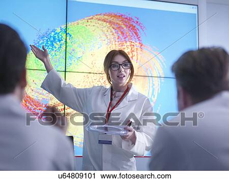 Stock Image - Female scientist making presentation in front of graphical display of silicon wafer on screens. Fotosearch