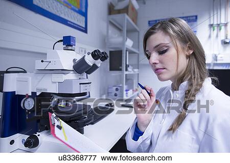 Stock Photo - Female scientist reading notes on clipboard in lab. Fotosearch