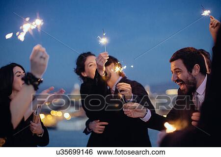 Stock Photograph - "Friends hugging and holding sparklers, at party". Fotosearch