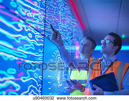 Stock Image - Geologists studying graphical display of oil and gas bearing rock on screens. Fotosearch