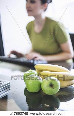 Stock Photography - "Green apples and bananas, young woman using computer in background". Fotosearch