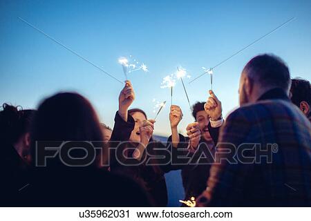 "Group of friends holding sparklers in air, at party" View Large Photo Image Stock Image - "Group of friends holding sparklers in air, at party". Fotosearch