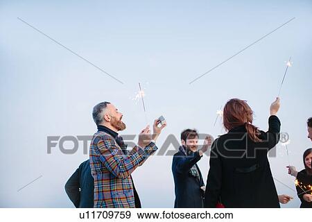 "Group of friends holding sparklers in air, at party" View Large Photo Image Stock Photo - "Group of friends holding sparklers in air, at party". Fotosearch
