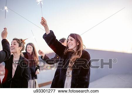 Stock Photo - "Group of friends holding sparklers in air, at party". Fotosearch