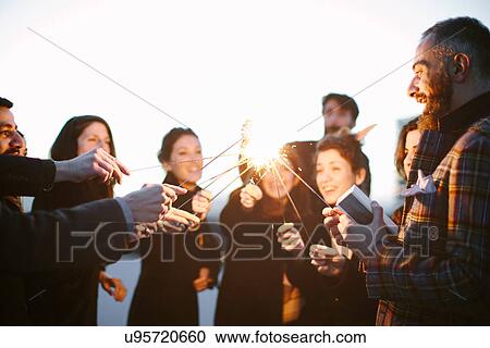 Stock Image - Group of friends touching sparklers at party. Fotosearch