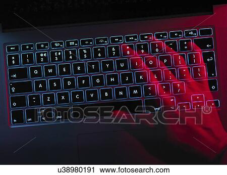 Stock Image - Hand working at laptop computer illustrating cyber crime. Fotosearch