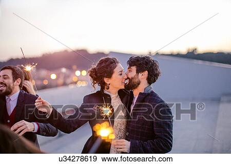 Stock Photo - Heterosexual couple holding sparklers and kissing at party. Fotosearch