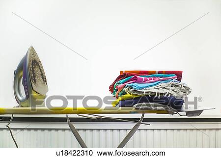 Stock Image - Iron and pile of laundry on ironing board. Fotosearch