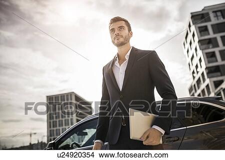 Picture - Low angle view of young businessman on street carrying digital tablet. Fotosearch