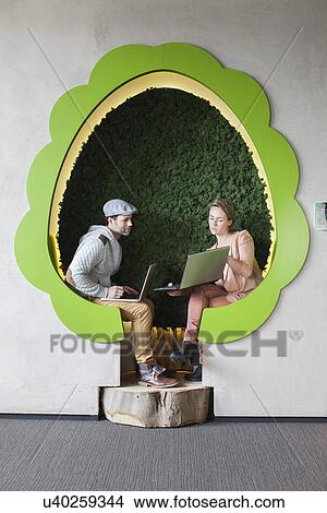 Picture - Male and female designers working on laptops in tree shaped office space. Fotosearch