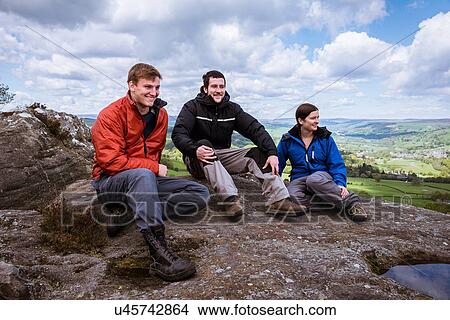 Picture - "Male and female hikers sitting on top of Guise Cliff, Pateley Bridge, Nidderdale, Yorkshire Dales". Fotosearch