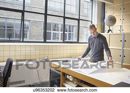 Stock Image - Male designer looking at blueprint in creative office. Fotosearch