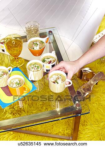 Stock Photography - Male hand picking up cup of Netherlands snert (pea soup) at retro party. Fotosearch