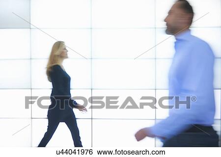 Stock Photograph - Man and woman walking past backlit wall panels. Fotosearch