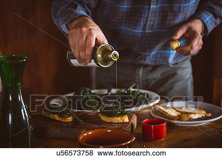 Stock Photo - Man pouring olive oil over Tuscan bruschetta and cavolo nero. Fotosearch