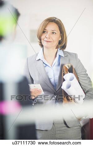 Stock Image - Mature businesswoman at meeting with smartphone and blueprints. Fotosearch