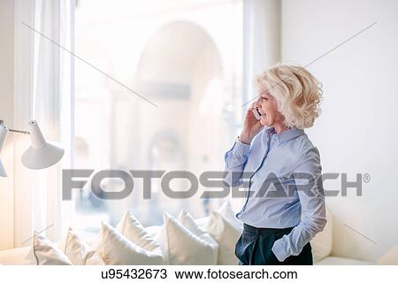 Stock Image - Mature businesswoman chatting on smartphone in office. Fotosearch