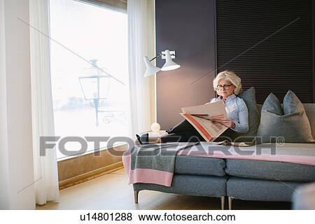 Stock Photo - Mature businesswoman reading newspaper on hotel room sofa. Fotosearch